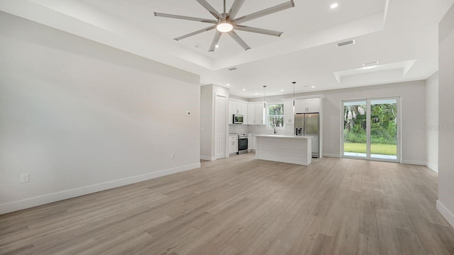 unfurnished living room with light hardwood / wood-style flooring, ceiling fan, and a tray ceiling