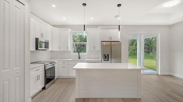 kitchen with sink, white cabinetry, decorative light fixtures, appliances with stainless steel finishes, and a kitchen island