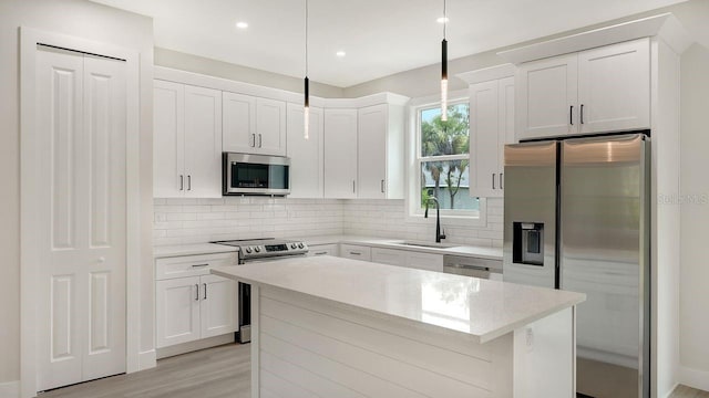 kitchen featuring sink, light hardwood / wood-style flooring, hanging light fixtures, stainless steel appliances, and white cabinets