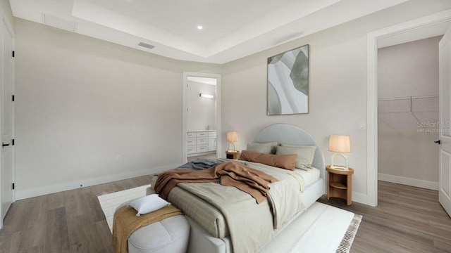 bedroom featuring a walk in closet, a raised ceiling, light hardwood / wood-style floors, and a closet