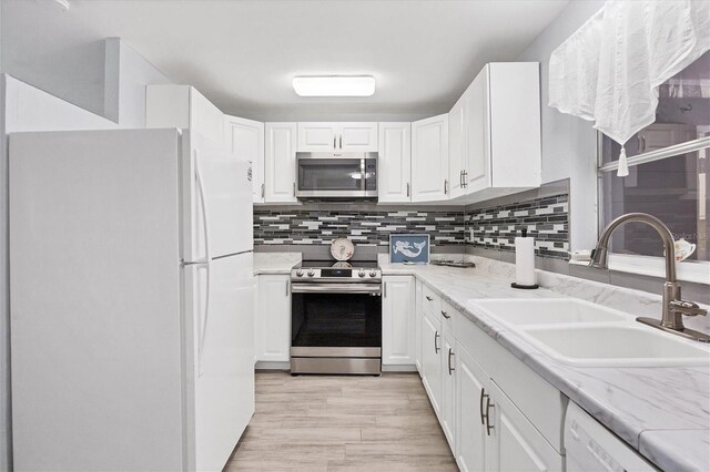 kitchen with appliances with stainless steel finishes, light stone counters, light hardwood / wood-style floors, white cabinetry, and sink