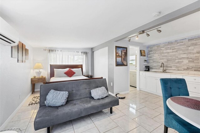 tiled bedroom featuring a wall unit AC, rail lighting, connected bathroom, and sink