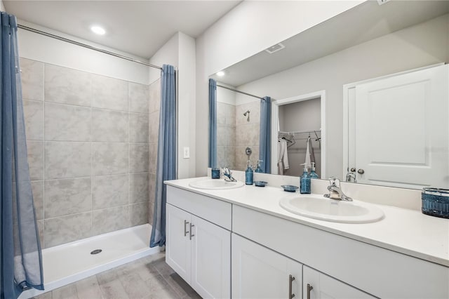 bathroom with double vanity, a stall shower, a spacious closet, and a sink