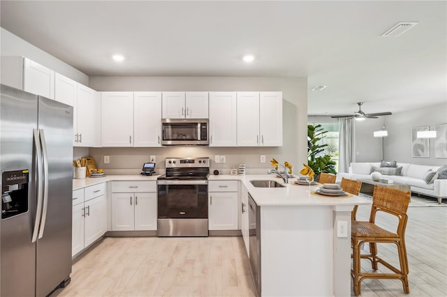 kitchen with light countertops, appliances with stainless steel finishes, open floor plan, a peninsula, and a kitchen breakfast bar