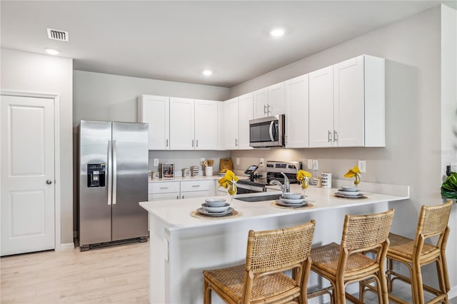 kitchen with a breakfast bar area, stainless steel appliances, white cabinetry, and kitchen peninsula