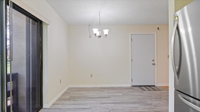 unfurnished dining area with baseboards, a textured ceiling, an inviting chandelier, and light wood-style flooring