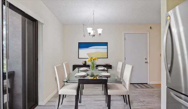 dining room with baseboards, a textured ceiling, an inviting chandelier, and light wood finished floors