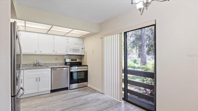 kitchen with white cabinets, light stone countertops, light wood-style floors, and stainless steel appliances