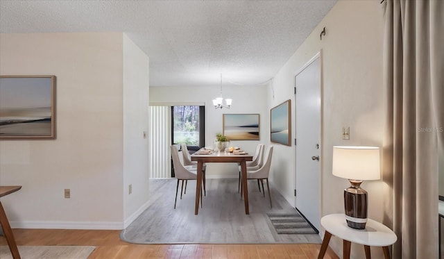 dining area with an inviting chandelier, wood finished floors, baseboards, and a textured ceiling