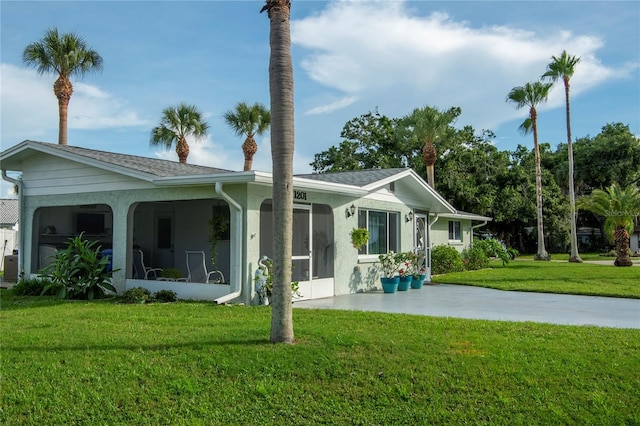 back of house featuring a yard, roof with shingles, a sunroom, and stucco siding