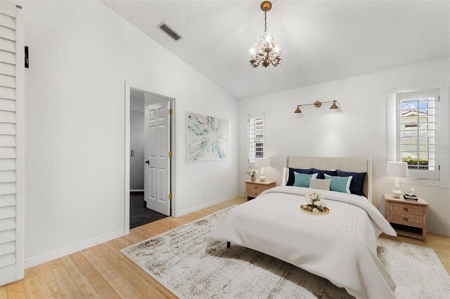 bedroom with hardwood / wood-style floors, vaulted ceiling, an inviting chandelier, and a textured ceiling