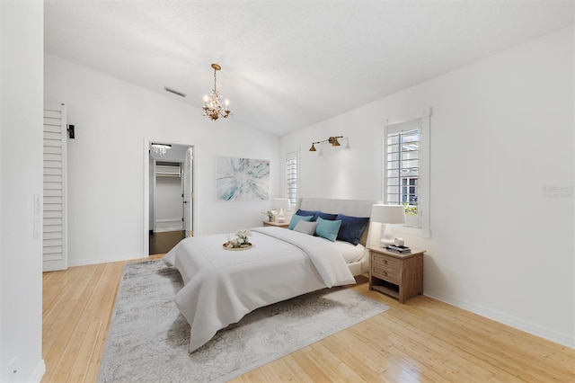 bedroom with a walk in closet, light hardwood / wood-style flooring, an inviting chandelier, lofted ceiling, and a closet