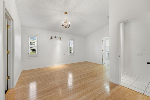 tiled spare room with a textured ceiling, a notable chandelier, and lofted ceiling