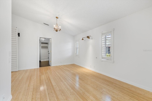 unfurnished room with vaulted ceiling, an inviting chandelier, and light wood-type flooring