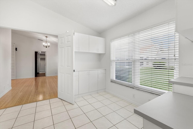 unfurnished room featuring vaulted ceiling, light tile patterned flooring, a healthy amount of sunlight, and a chandelier