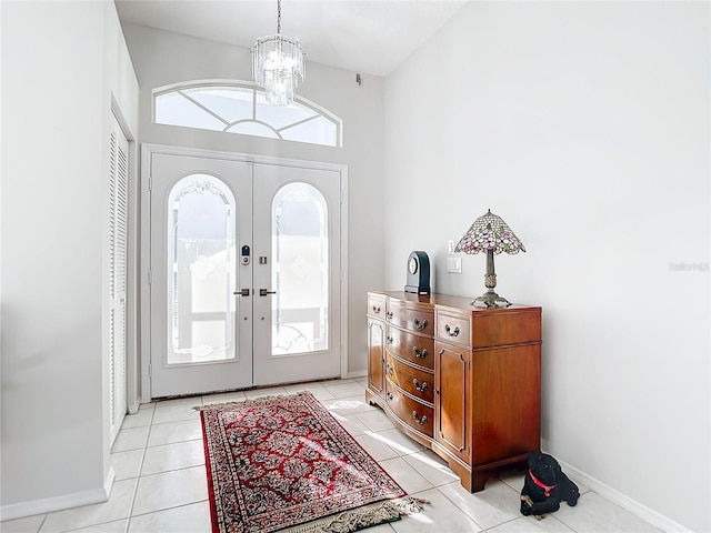 tiled foyer entrance with a high ceiling, a chandelier, and french doors