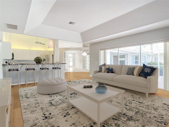 living room featuring a raised ceiling, ceiling fan, a textured ceiling, and light wood-type flooring