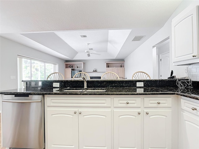 kitchen with white cabinetry, stainless steel dishwasher, a raised ceiling, and dark stone counters