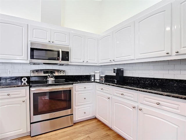 kitchen with light hardwood / wood-style flooring, stainless steel appliances, dark stone counters, and white cabinets