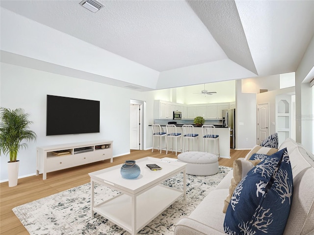 living room with ceiling fan, a textured ceiling, light hardwood / wood-style floors, and a tray ceiling