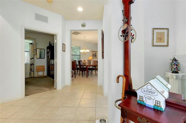 hall with light tile patterned floors, light colored carpet, visible vents, baseboards, and an inviting chandelier