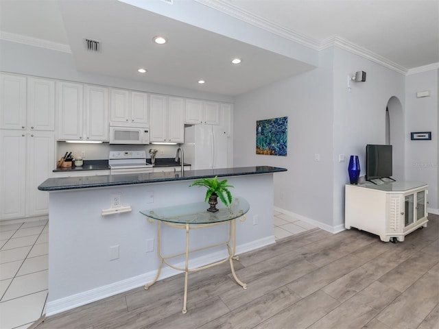 kitchen featuring white appliances, ornamental molding, a large island with sink, and white cabinets