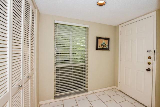 entryway featuring a textured ceiling, light tile patterned floors, and baseboards