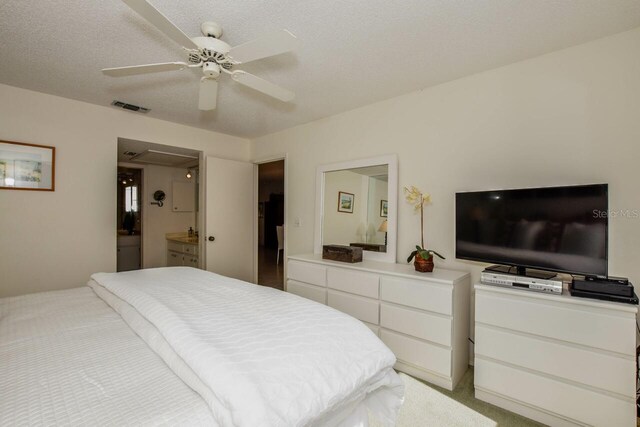 bedroom with light colored carpet, ensuite bathroom, a textured ceiling, and ceiling fan