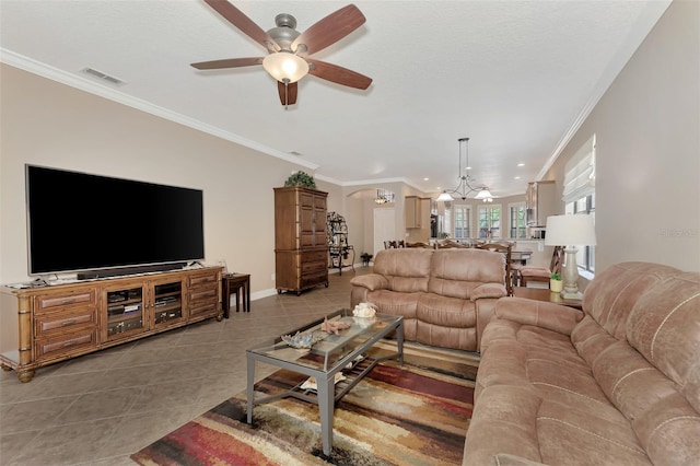 living area featuring tile patterned flooring, ceiling fan with notable chandelier, visible vents, baseboards, and crown molding