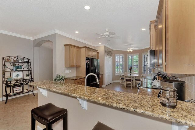 kitchen featuring ceiling fan, crown molding, light stone countertops, and stainless steel fridge