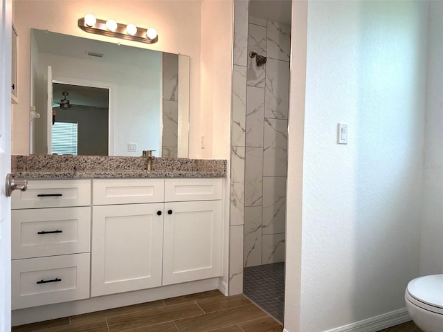 bathroom with a tile shower, vanity, toilet, and ceiling fan