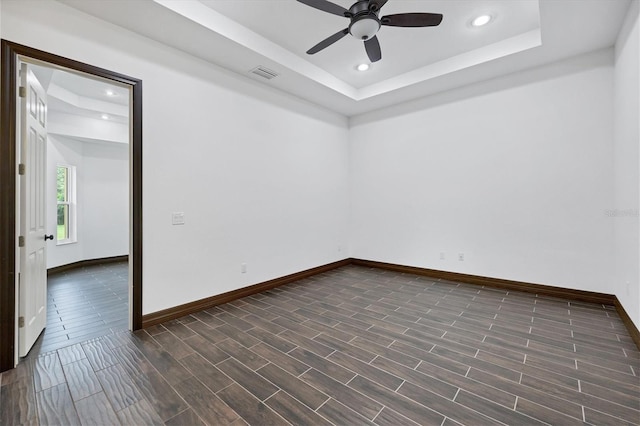 spare room featuring ceiling fan, dark hardwood / wood-style floors, and a tray ceiling