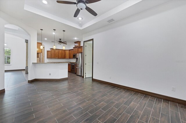 unfurnished living room with dark wood-type flooring, ceiling fan, and a raised ceiling