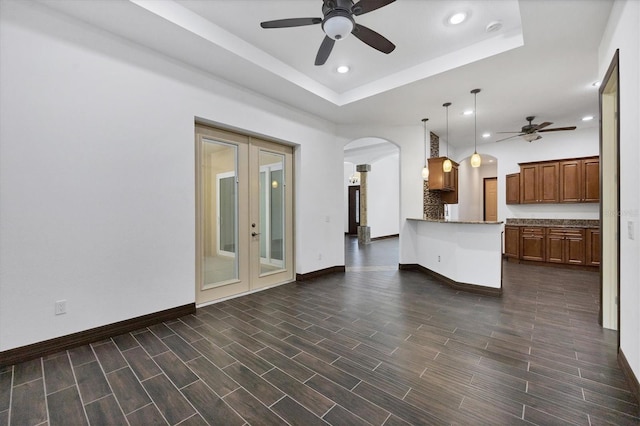 unfurnished living room featuring a raised ceiling, french doors, dark hardwood / wood-style flooring, and ceiling fan