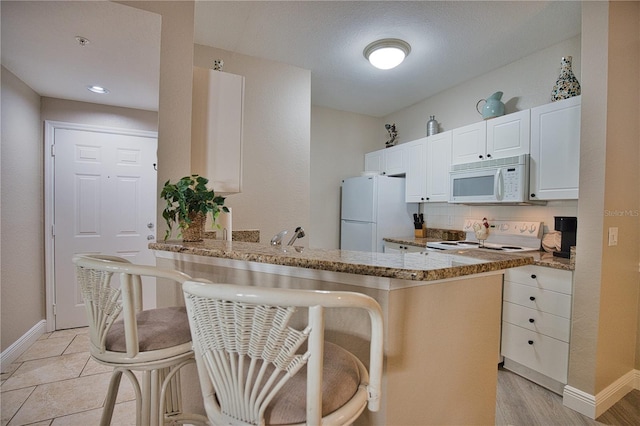 kitchen with white cabinets, white appliances, light hardwood / wood-style flooring, stone countertops, and kitchen peninsula