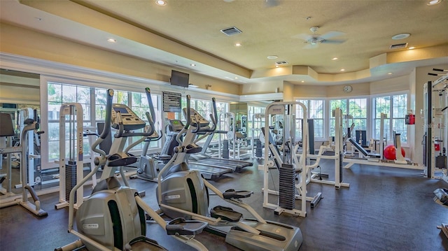 workout area with a tray ceiling, ceiling fan, and a healthy amount of sunlight