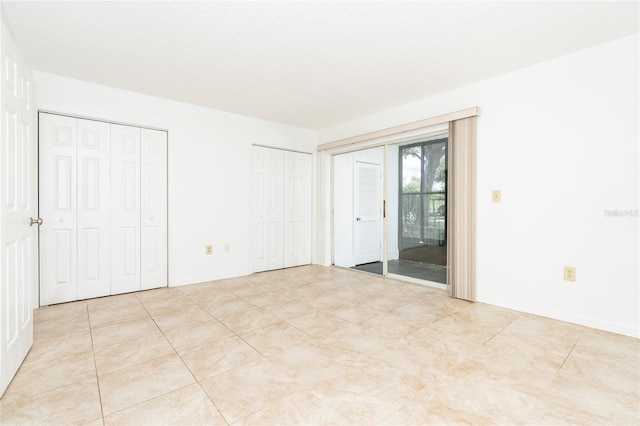 unfurnished bedroom with a textured ceiling, access to outside, light tile patterned floors, and two closets