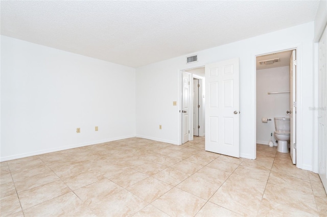 unfurnished bedroom featuring ensuite bathroom, a textured ceiling, and light tile patterned floors