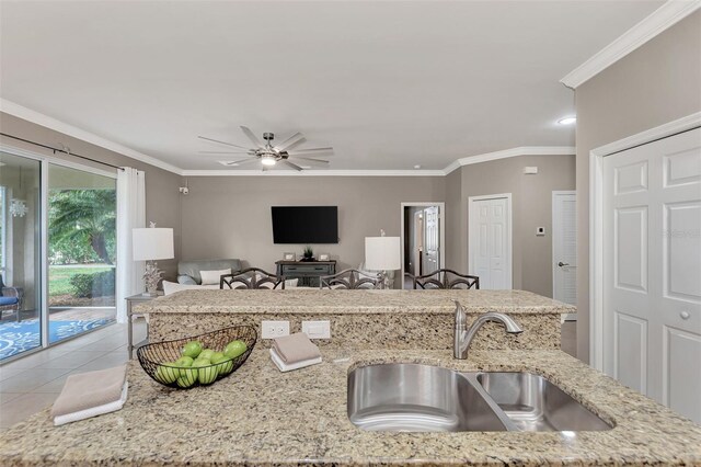 kitchen with sink, light tile patterned floors, crown molding, light stone countertops, and ceiling fan