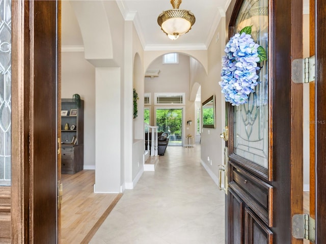 foyer entrance with light wood finished floors, baseboards, ornamental molding, and arched walkways