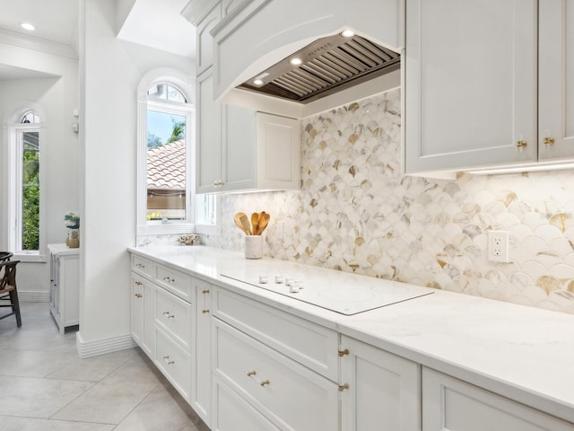 kitchen with light tile patterned floors, white electric stovetop, custom range hood, white cabinetry, and backsplash