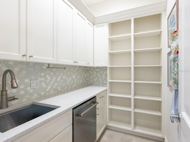 kitchen featuring stainless steel dishwasher, tasteful backsplash, white cabinetry, light tile patterned floors, and sink