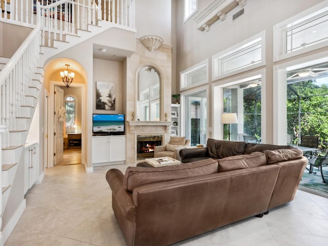 tiled living room with a high ceiling, plenty of natural light, ceiling fan with notable chandelier, and a high end fireplace