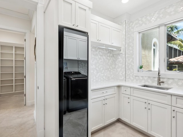 kitchen featuring washing machine and clothes dryer, tasteful backsplash, light countertops, white cabinetry, and a sink