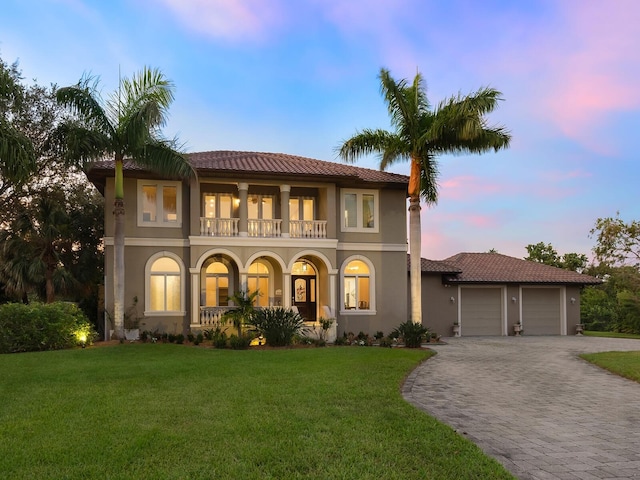 mediterranean / spanish-style home featuring decorative driveway, a yard, stucco siding, an attached garage, and a balcony