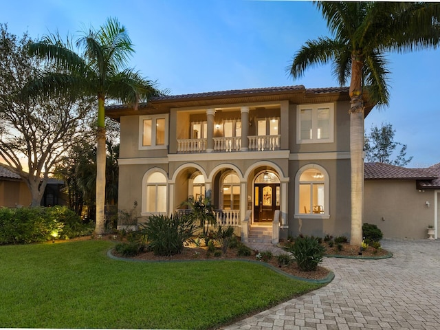 mediterranean / spanish-style house with a balcony, covered porch, decorative driveway, stucco siding, and a front yard