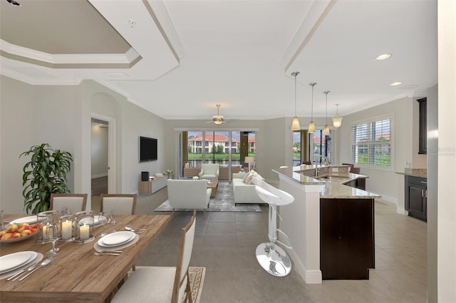 kitchen featuring light stone countertops, sink, ceiling fan, an island with sink, and pendant lighting