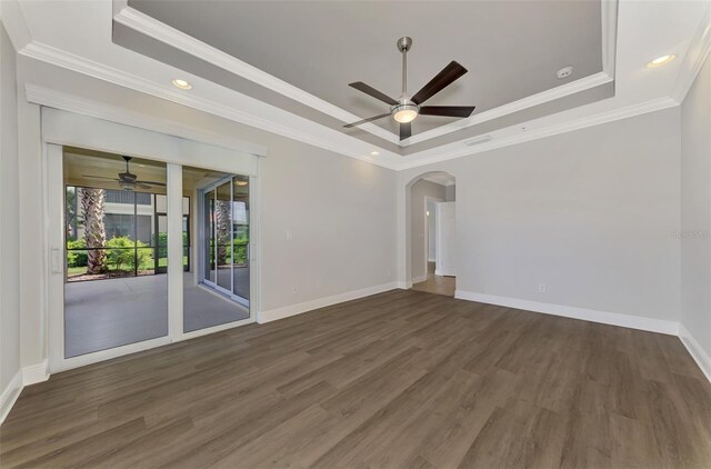 spare room with ornamental molding, a tray ceiling, ceiling fan, and dark wood-type flooring