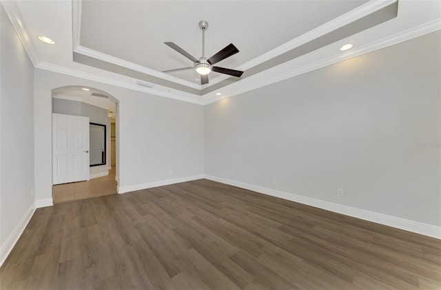 empty room featuring a tray ceiling, dark wood-type flooring, ornamental molding, and ceiling fan