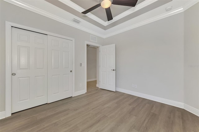 unfurnished bedroom with ceiling fan, a raised ceiling, light hardwood / wood-style floors, a closet, and ornamental molding